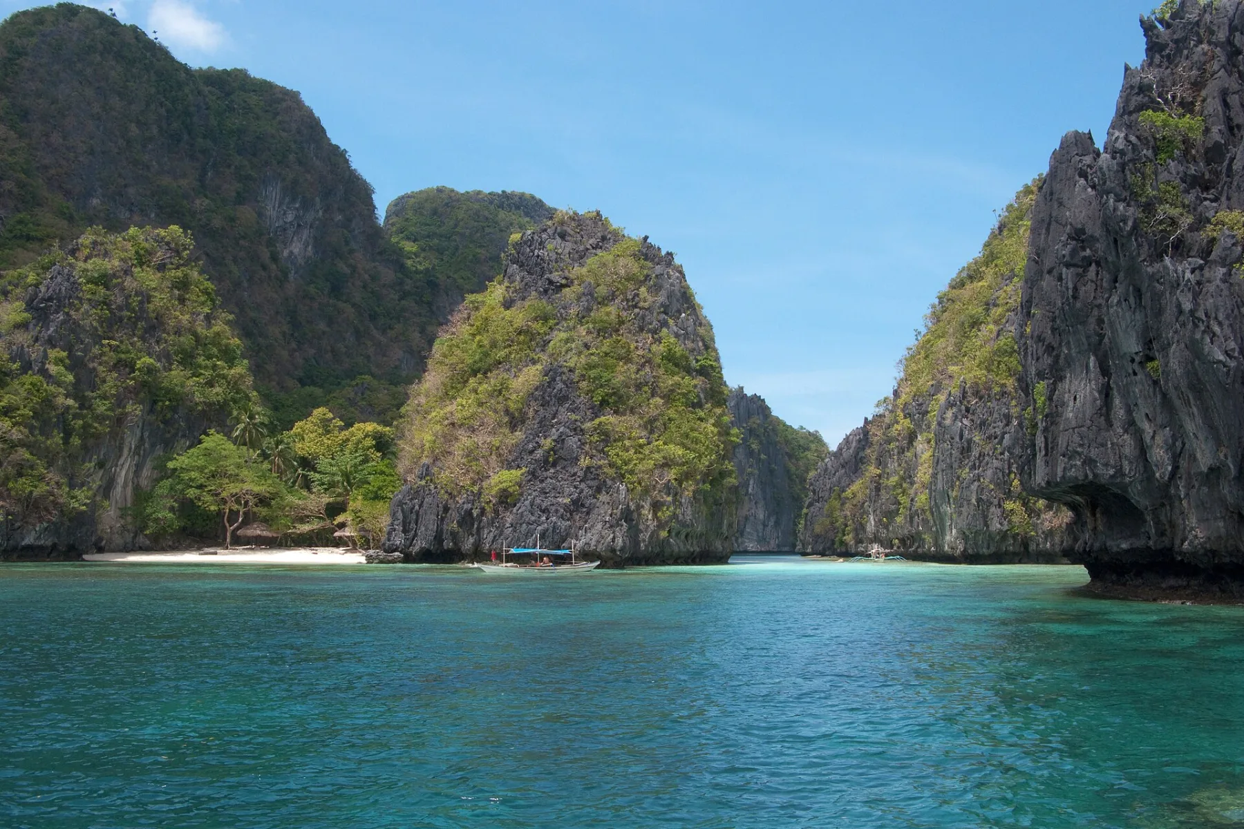 Kalksteenwanden omringen een bangka-boot in de turquoise lagune van de Bacuit Bay, El Nido, Palawan